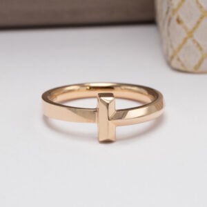 Upea Tiffany & Co. T-sormus, joka on valmistettu 18 karaatin keltakullasta. Tämä ikoninen koru edustaa Tiffanyn tunnistettavaa muotoilua.