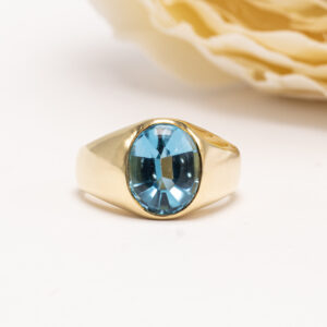 Upea 18 karaatin keltakultainen topaasisormus, jonka keskiössä loistaa ovaali sekahiontainen vaaleansininen topaasi.