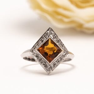 Helsingissä vuonna 1993 valmistettu uniikki sitriinisormus, jonka keskiössä loistaa neliön muotoon viistehiottu oranssinkeltainen sitriini.