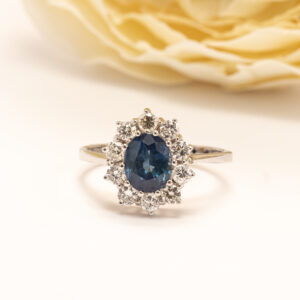 Valkokultainen safiiri- timanttisormus, jossa Dianasormus tyylinen klassinen kukkakehä tuo koruun arvokkuutta ja ajattomuutta.