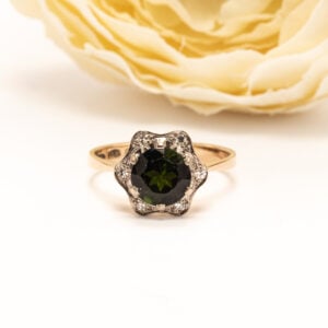 Sormuksen keskipisteenä säihkyy pyöreä viistehiottu turmaliini (2 ct), jonka syvä vihreä sävy tuo koruun persoonallisuutta ja arvokasta ilmettä.