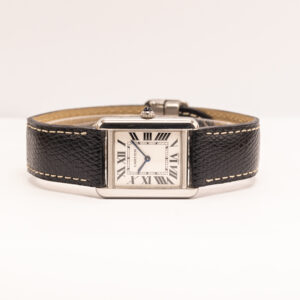 Cartier Tank on yksi kellomaailman tunnetuimmista ja pitkäikäisimmistä muotoiluikoneista. Louis Cartier suunnitteli ensimmäisen Tank-kellon vuonna 1917, ja sen suoraviivainen geometria sai inspiraationsa ensimmäisen maailmansodan aikaisista panssarivaunuista. Mallin suorakulmainen kuori, roomalaiset numerot, sinistetyt osoittimet ja cabochon-koristeinen nuppi ovat muodostaneet tunnistettavan ilmeen, joka on säilynyt osana Cartierin mallistoa jo yli vuosisadan. Tässä Cartier Tankissa on ruostumattomasta teräksestä valmistettu 24 × 31 mm:n kuori. Vaaleaa kellotaulua kehystävät suuret mustat roomalaiset numerot, ja siniset osoittimet tuovat kokonaisuuteen Cartierille tunnusomaista kontrastia. Klassiset mittasuhteet tekevät kellosta sirosti ranteeseen asettuvan ja ajattoman vaihtoehdon niin arkeen kuin juhlavampaankin käyttöön. Kellossa on tarkka ja helppokäyttöinen kvartsikoneisto. Kelloon on asennettu uusi musta Cartierin nahkaranneke, joka täydentää Tank-mallin klassista mustavalkoista ilmettä. Cartier Tank on säilyttänyt asemansa yhtenä arvokellojen tunnetuimmista designklassikoista. Pelkistetty suorakulmainen muotoilu on tehnyt mallista poikkeuksellisen ajattoman, ja se on ollut vuosikymmenten aikana sekä miesten että naisten suosima pukukello. Kello toimitetaan Cartierin säilytyskotelon kanssa.