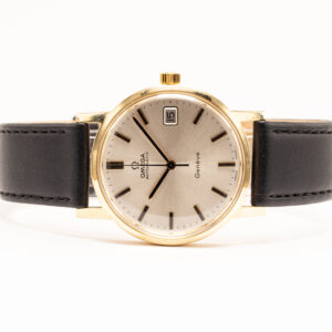 Omega Genève -mallisto oli erityisesti 1960- ja 1970-luvuilla tärkeä osa Omegan valikoimaa. Genève-nimi viittasi sveitsiläisen kellonvalmistuksen keskeiseen kaupunkiin, ja malliston kellot tunnettiin selkeästä muotoilustaan sekä laadukkaista mekaanisista koneistoistaan. Nykyään aikakauden Genève-kellot ovat kiinnostavia vintage-Omegoita, joissa ajan tyyli näkyy hillityllä tavalla. Tämä vuonna 1973 valmistettu Omega Genève on halkaisijaltaan 34 mm, ja sen kuori on valmistettu 14 karaatin keltakullasta. Vaaleassa, hienovaraisesti säteittäisharjatussa kellotaulussa on tummasävyiset kullanväriset indeksit ja osoittimet. Päivämääränäyttö sijaitsee kello kolmen kohdalla. Pelkistetty kellotaulu, ohut kultainen kehys ja tumma nahkaranneke muodostavat klassisen 1970-luvun kokonaisuuden. Kellossa on automaattinen mekaaninen koneisto, joten se vetää käyntivoimansa ranteen liikkeestä. Kellotaulun alkuperäistä aikakautta henkivä typografia ja lämminsävyinen 14 karaatin kultakuori tekevät kellosta hienon esimerkin yli 50 vuotta vanhasta Omega-vintagekellosta. Kellolle on tehty täyshuolto huhtikuussa 2026.