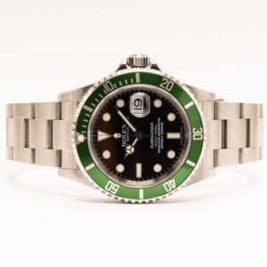 Rolex Submariner on yksi maailman tunnetuimmista sukelluskelloista ja sveitsiläisen kellonvalmistuksen arvostetuimmista klassikoista. Vuonna 1953 esitelty Submariner suunniteltiin alun perin ammattisukeltajien käyttöön, mutta vuosikymmenten aikana siitä on tullut myös yksi Rolexin halutuimmista kellomalleista. Submarinerin tunnistettava muotoilu, tekninen luotettavuus ja vahva historia ovat tehneet siitä ajattoman suosikin niin kelloharrastajien kuin keräilijöiden keskuudessa. Tämä vuonna 2007 valmistettu Rolex Submariner Date on erityisen kiinnostava versio malliston historiassa. Kellossa on musta kellotaulu ja näyttävä vihreä alumiininen sukeltajankehä, joiden yhdistelmä tunnetaan kelloharrastajien keskuudessa lempinimellä Kermit. Vihreäkehäinen Submariner esiteltiin vuonna 2003 malliston 50-vuotisjuhlavuoden kunniaksi, ja siitä muodostui nopeasti yksi Submariner-malliston tunnistettavimmista erikoisversioista. Kellon ruostumattomasta teräksestä valmistetun Oyster-kuoren halkaisija on 40 mm. Sen mittasuhteet edustavat perinteistä Submariner-muotoilua, jossa sporttinen rakenne yhdistyy tasapainoiseen istuvuuteen ranteessa. Mustaa kellotaulua koristavat selkeät, luminoidut tunti-indeksit ja Rolexin tunnusomaiset Mercedes-osoittimet. Päivämääränäyttö sijaitsee kello kolmen kohdalla, ja sen lukemista helpottaa Cyclops-suurennuslasi. Kellossa on automaattinen, kronometrisertifioitu koneisto. Submarinerin yksisuuntaisesti pyörivä sukeltajankehä on suunniteltu sukellusajan seuraamiseen, ja mallin vesitiiviysluokitus on 300 metriä. Vankkarakenteinen Oyster-ranneke täydentää kellon sporttista ja ajatonta kokonaisuutta. Vihreäkehäinen Submariner on saavuttanut erityisen aseman Rolex-keräilijöiden keskuudessa. Sen valmistus ajoittuu aikaan ennen vuonna 2010 esiteltyä keraamikehäistä Submariner-sukupolvea, mikä tekee alumiinikehäisestä Kermit-mallista kiinnostavan osan Rolexin sukelluskellojen historiaa. Kellolle on tehty täyshuolto toukokuussa 2020. Kello toimitetaan alkuperäisessä Rolex-kotelossa alkuperäisten papereiden sekä huoltotodistuksen kanssa. Alkuperäisten asiakirjojen ja kotelon säilyminen on arvostettu ominaisuus erityisesti keräilykelloissa.